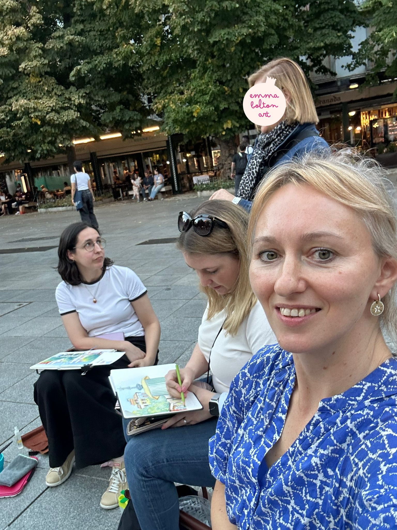 Two white women sketching in Bib Rambla, while a third takes a selfie.  The woman on the left is looking up apprehensively at an older woman with a leopard-print scarf.