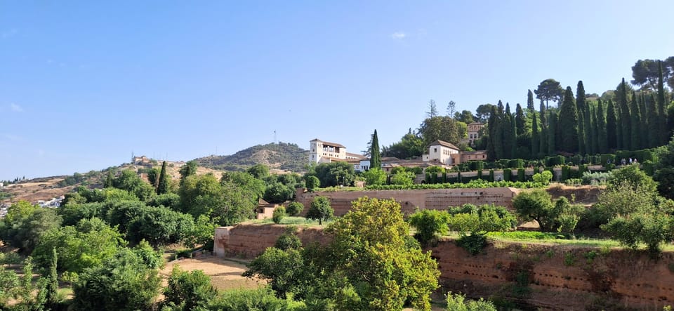 View of a beautiful white palace on the side of a hill under a blue sky. It's surrounded by greenery.